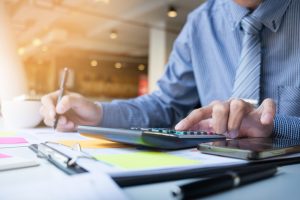 Professional accountant calculating financial figures on a calculator while reviewing documents and digital records at an office desk, illustrating Corporate Tax planning, compliance, and financial management for businesses.
