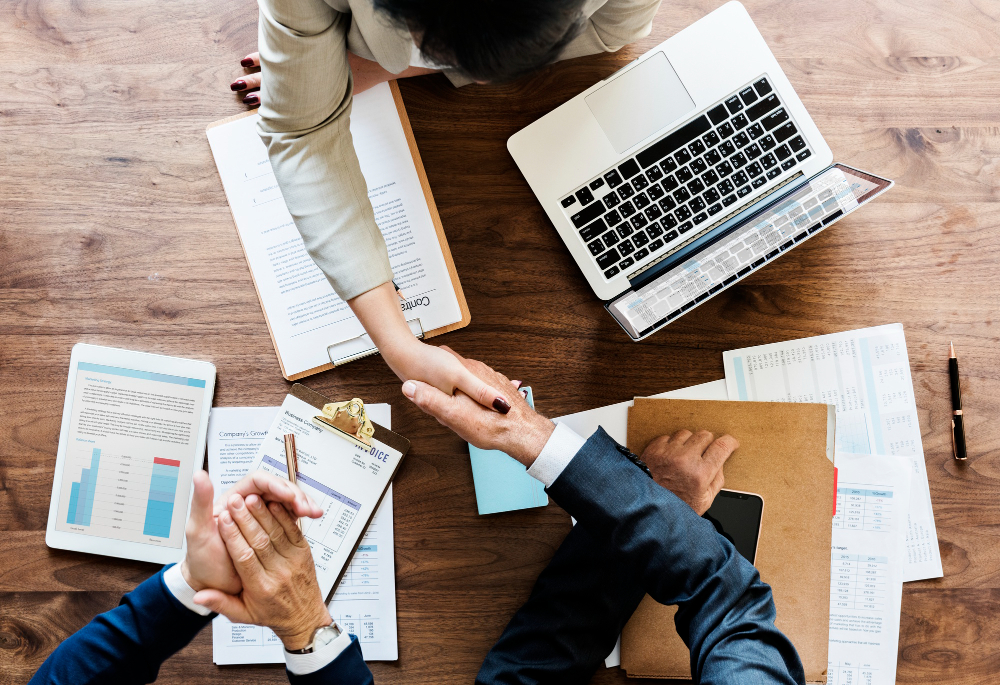 Business professionals shaking hands over financial documents and reports during a corporate meeting, representing compliance with UAE Transfer Pricing Laws, tax documentation, and strategic business planning.