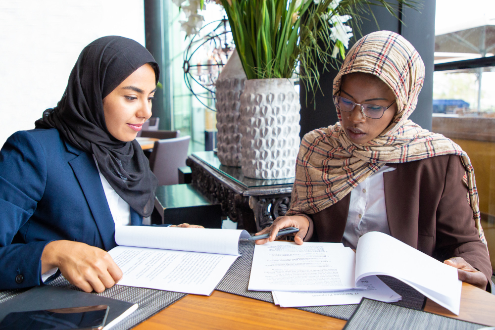 Two business professionals reviewing financial documents and discussing reports in a modern office setting, representing Accounting in UAE, financial record management, compliance, and business advisory services.
