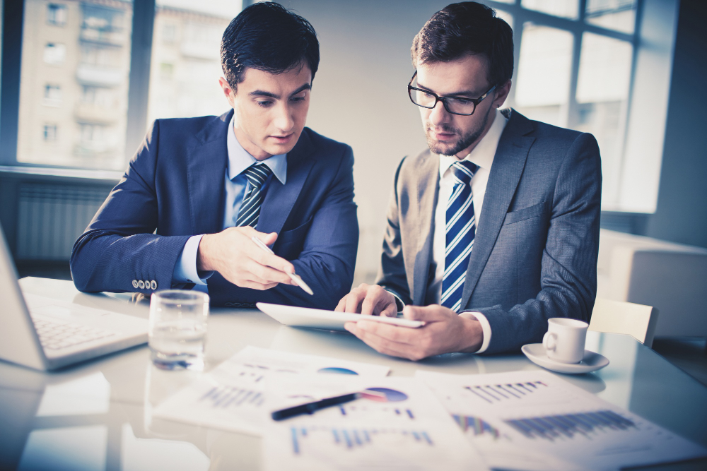 Business professionals reviewing financial reports and performance data on a tablet during a meeting, highlighting the importance of Audit for UAE Businesses to ensure compliance, transparency, and informed decision-making.