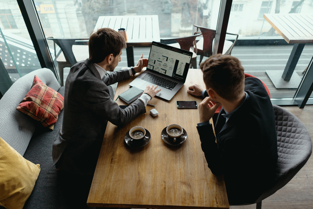 Two business professionals reviewing financial dashboards and strategic plans on a laptop during a meeting, supporting business setup with financial planning, market analysis, and business growth strategies.
