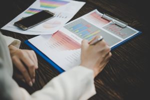 Professional reviewing financial charts, performance data, and business analytics on printed documents, highlighting the importance of an MIS Report for business performance monitoring, financial analysis, and informed decision-making.